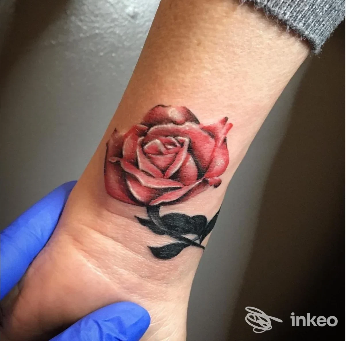 Tatuaggio realistico di rosa rossa sull’avambraccio/caviglia, visibile senza volti, eseguito sul corpo, senza overlay o schermo.
