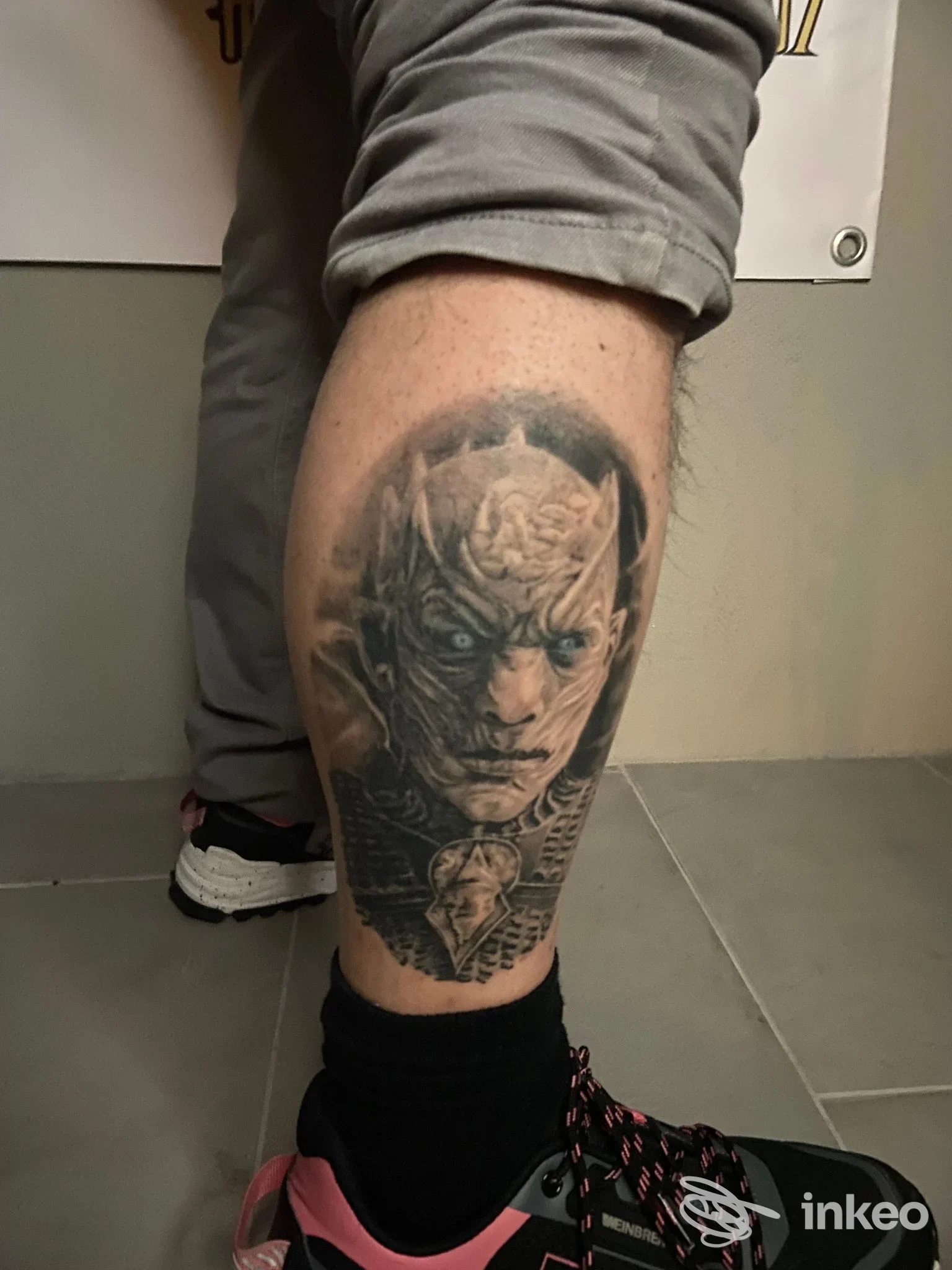 Tattoo realistico su gamba di una figura con volto minuzioso, visibile chiaramente sulla pelle; nessun overlay o testo visibile.