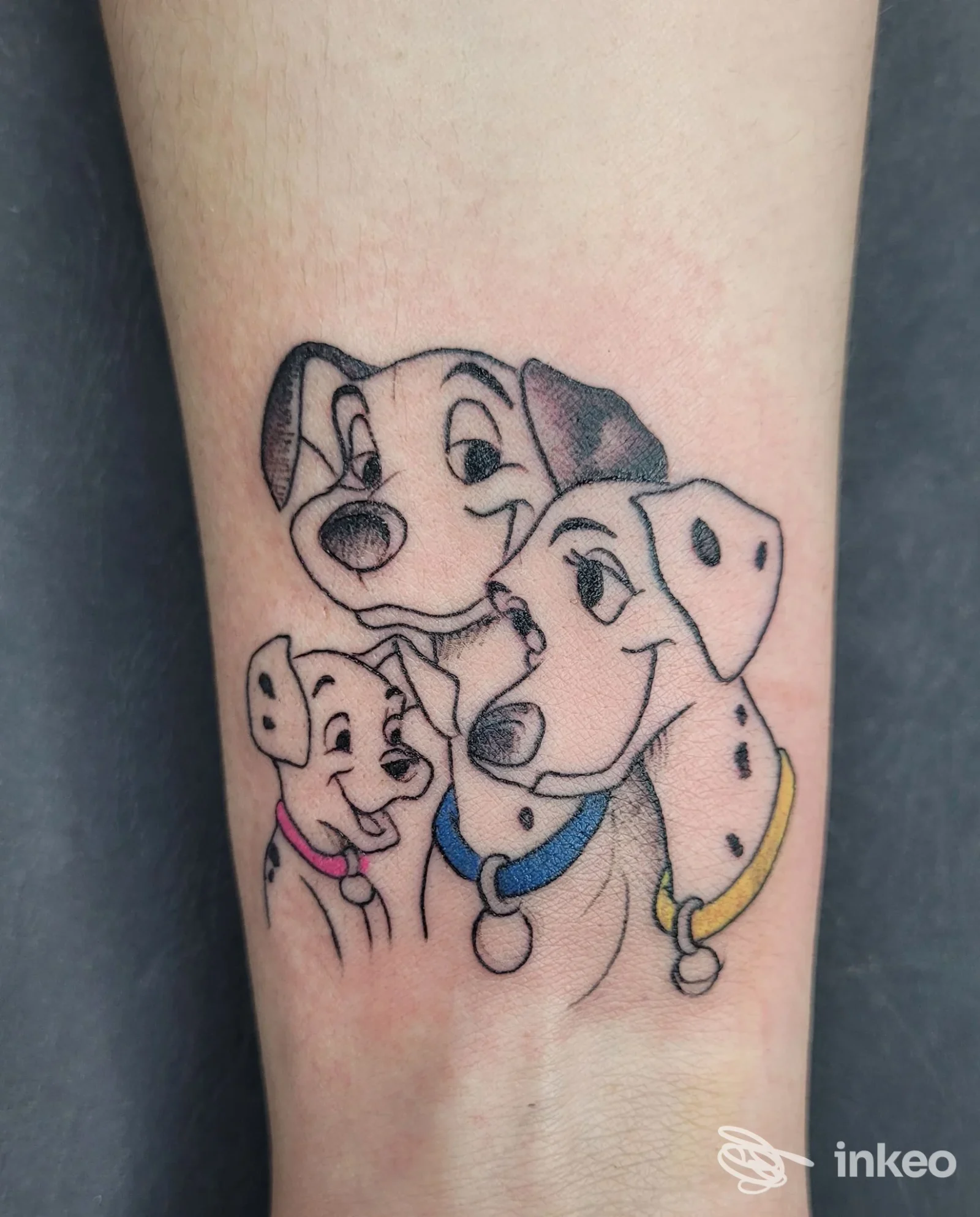 Tattoo su pelle sull'avambraccio sinistro che mostra tre cuccioli di cani con contorni neri e riempimenti: un'opera tatuata chiaramente su pelle reale, senza testi o watermark visibili.