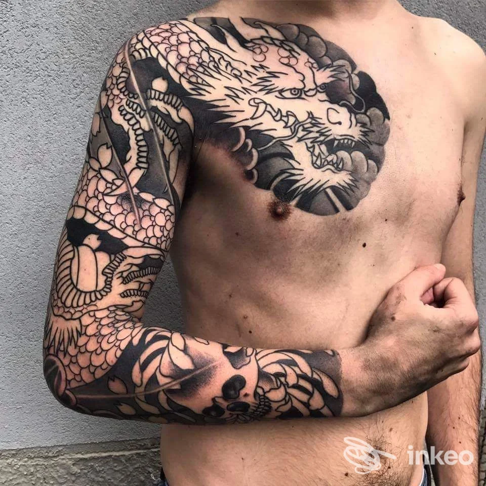 Tattooing su torace e braccio sinistro: grande braccio con disegno scuro, stile tradizionale, visibile in primo piano.