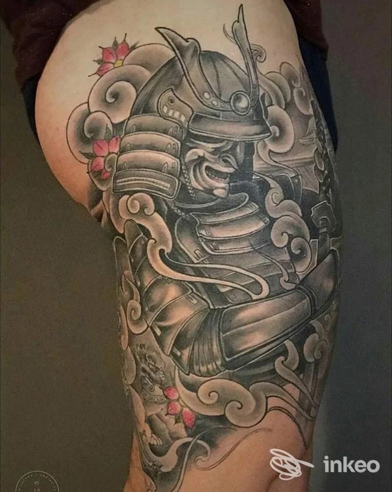 Tattoo samurai in stile traditional giapponese su coscia, con armatura e nuvole, tonalità nere e grigie con accenti rosa sui fiori.