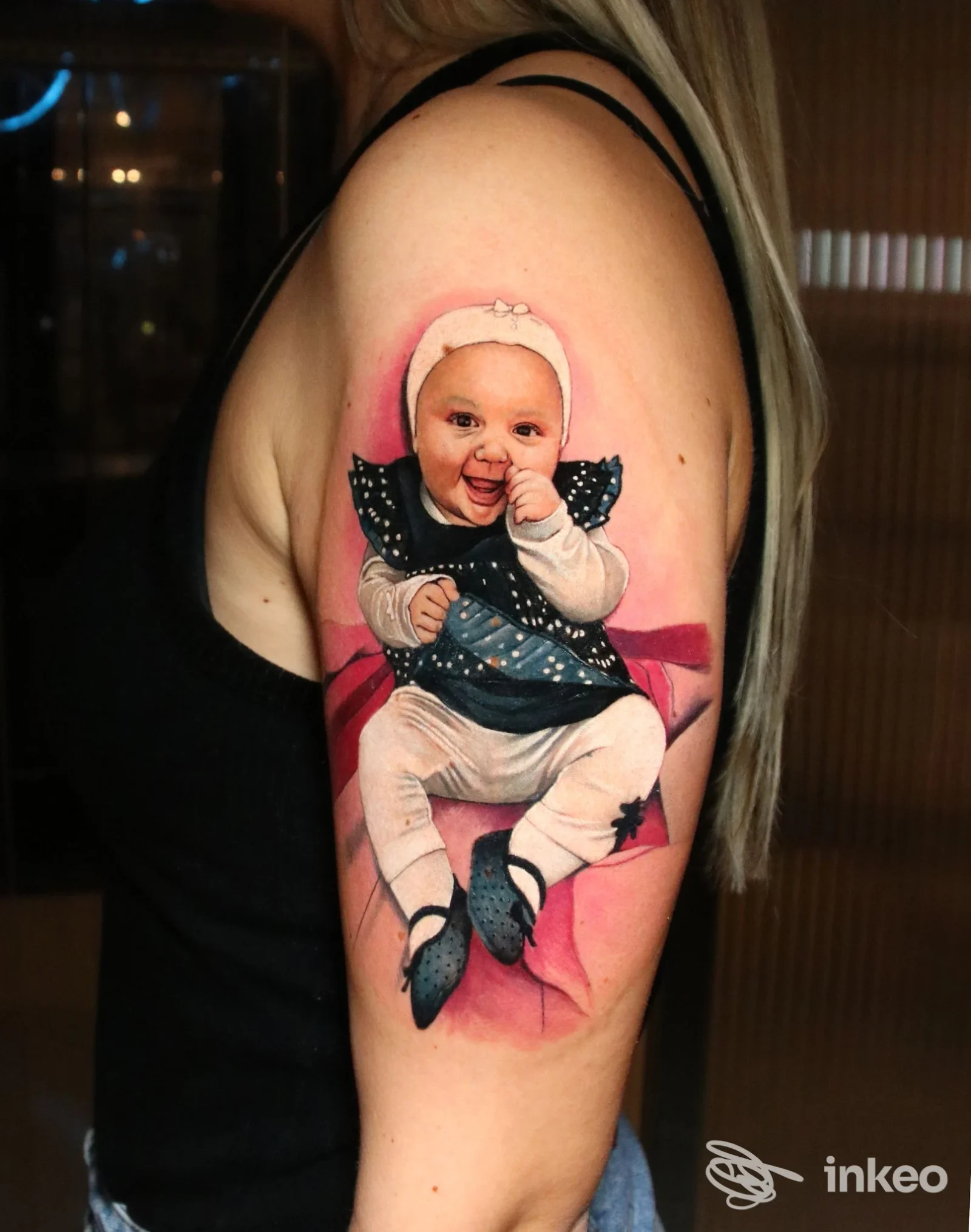 Tatù realistico sull’avambraccio sinistro raffigurante un bambino sorridente, con sfondo rosa, su pelle reale. Studio: L'Arte del Tatuaggio, città non specificata.