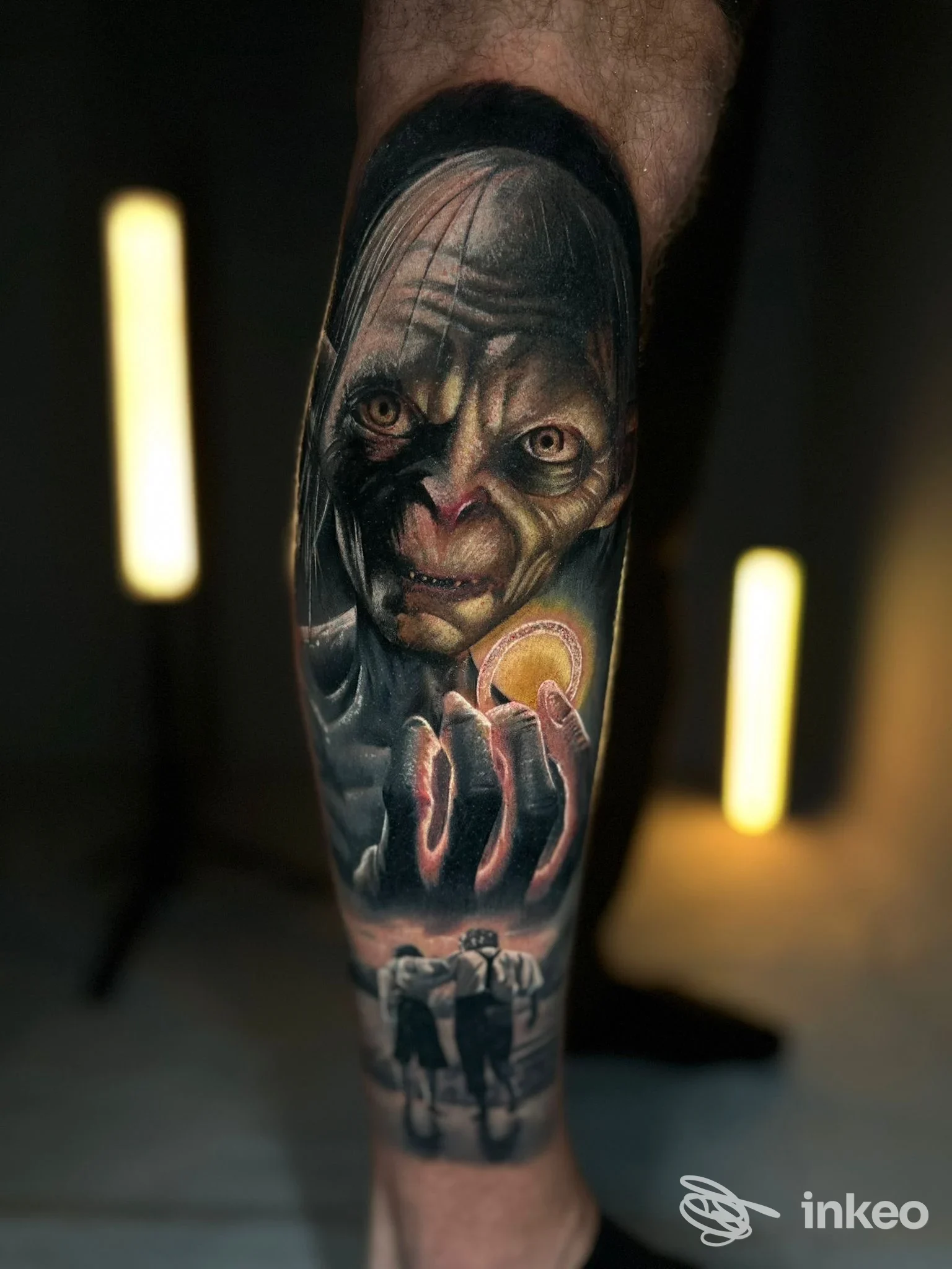 Tatuaggio realistico sulla gamba raffigurante una creatura con grandi occhi che tiene una sfera gialla; in basso si intravedono due figure in bianco e nero in un contesto notturno.