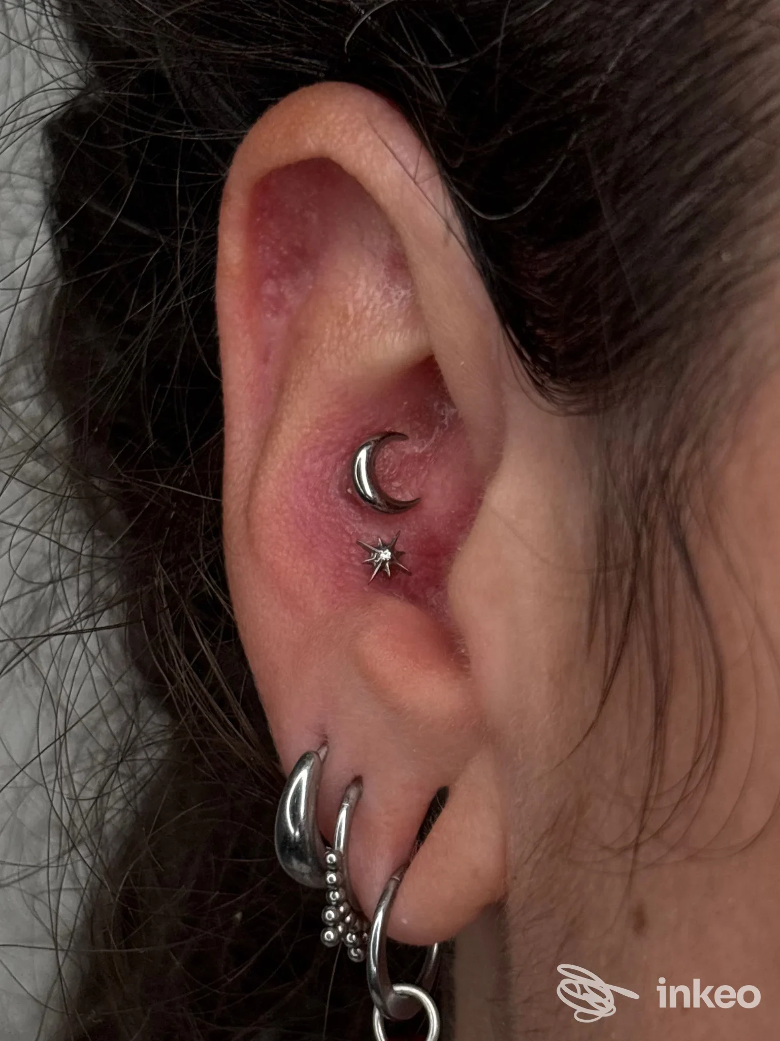 Piercing multipli sull’orecchio sinistro con anello a ferro di cavallo, pendente stellato e altri gioielli lungo il lobo, visibili in primo piano.
