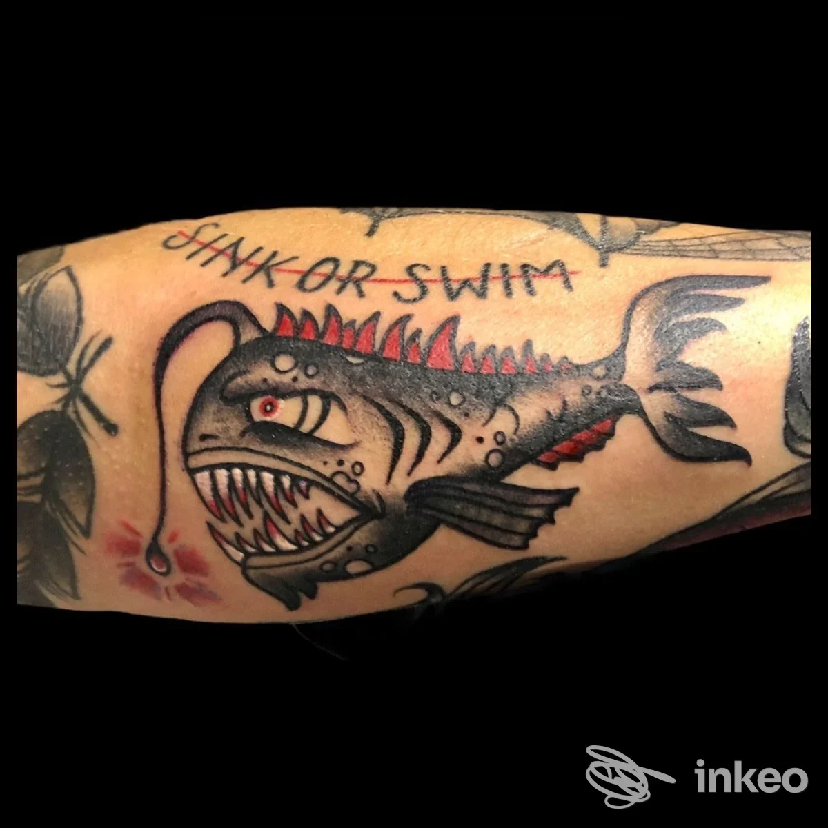Tatuaggio raffigurante uno squalo su braccio, con denti affilati e pinna dorsale rossa, stile cartoonesco, colori neri e rossi ben definiti.