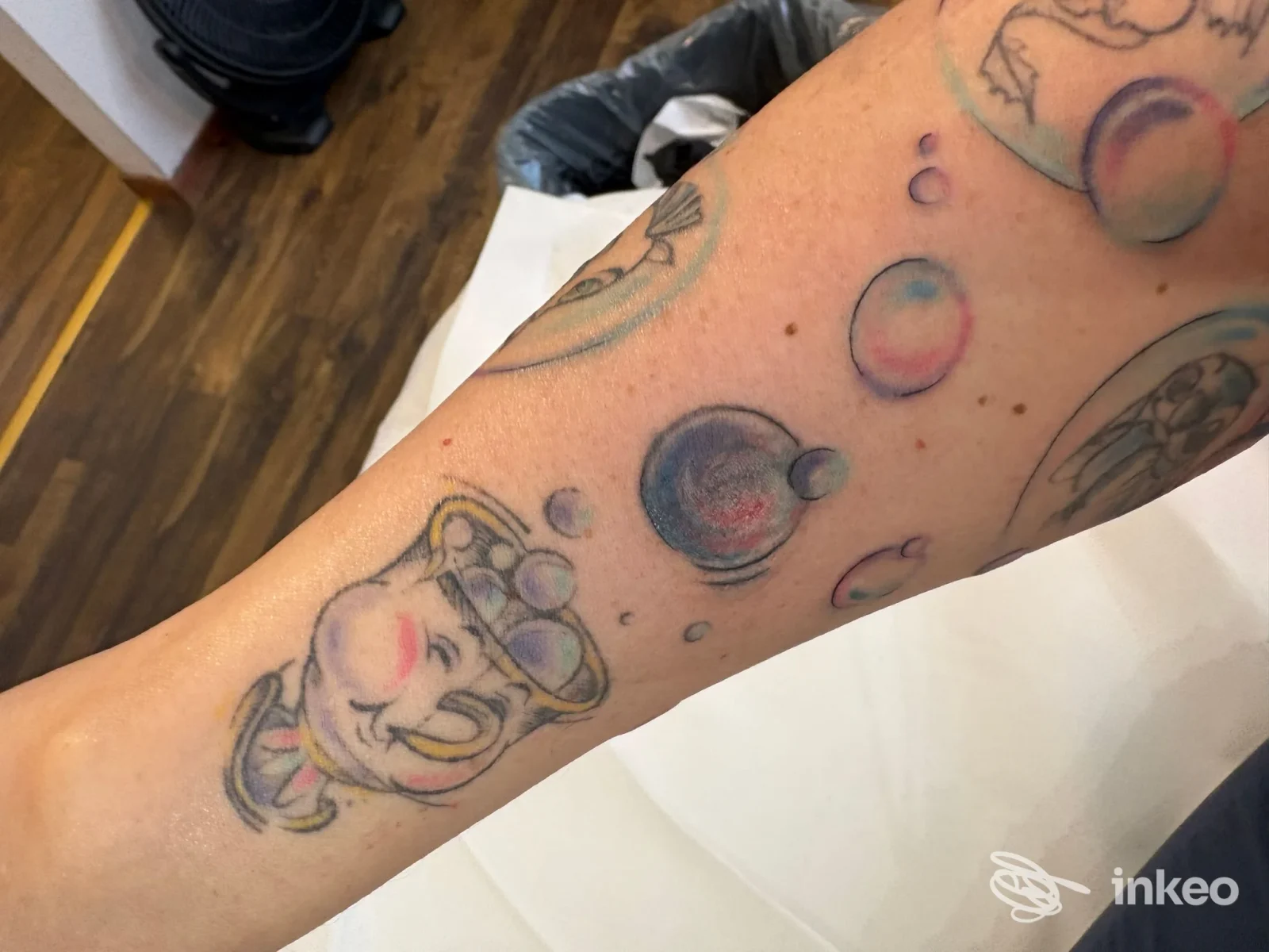 Braccio sinistro con tatuaggi colorati: figura cartoonesca e sfere colorate, senza viso visibile, scatto in studio.