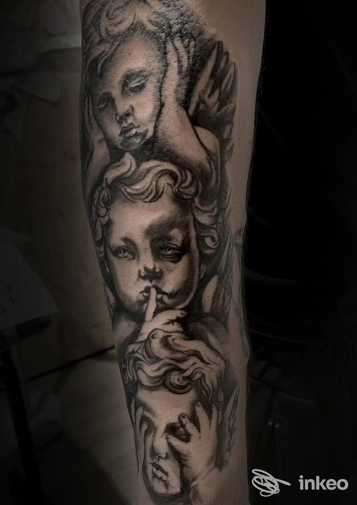 Tattoo in bianco e nero su avambraccio raffigurante volti angelici intrecciati, eseguito direttamente sulla pelle, con dettagli e linee nette.