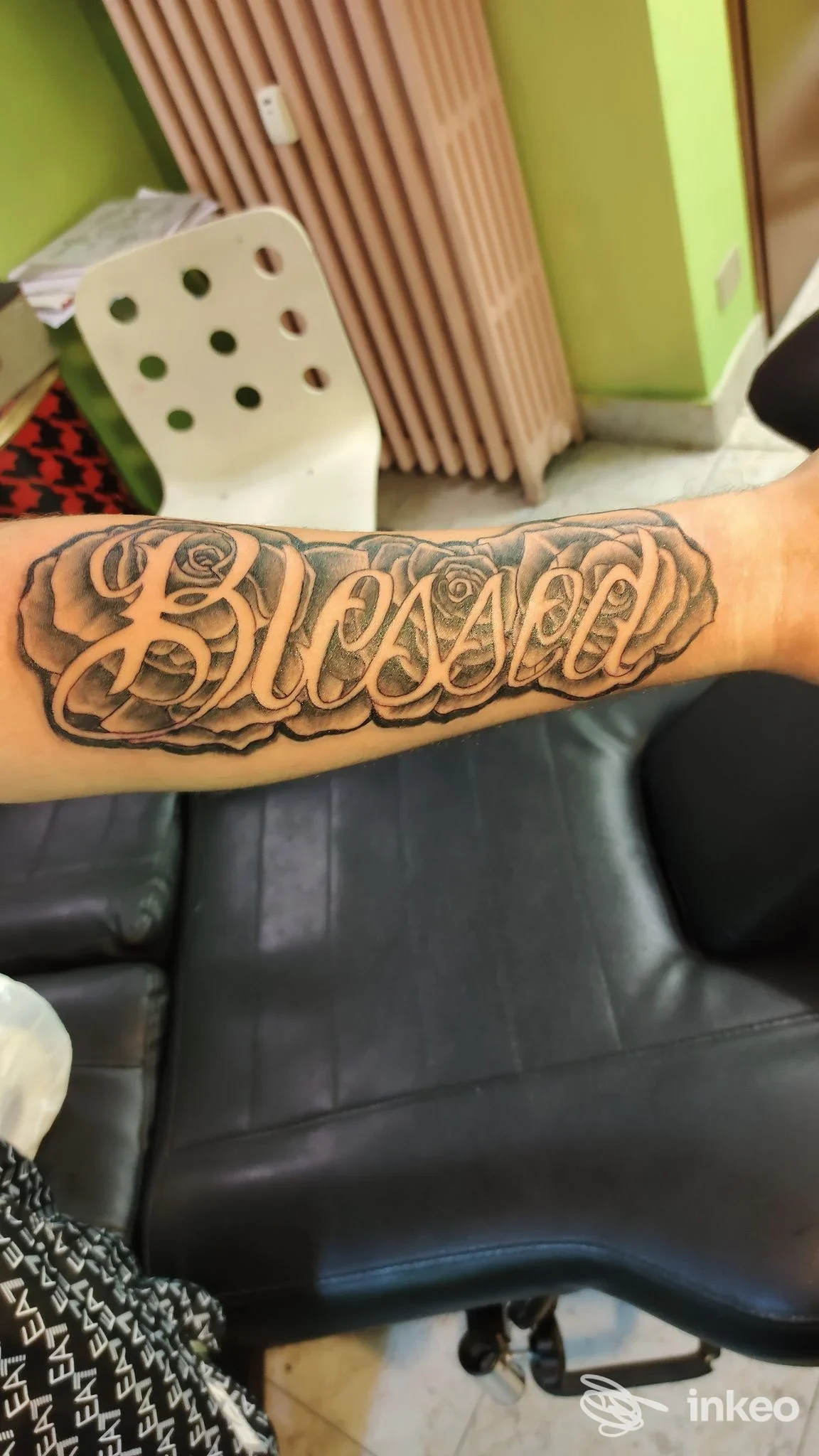 Braccio di una persona con tatuaggio in stile lettering ‘Blessed’ ben visibile sull’avambraccio, contorni scuri e riempimento denso.