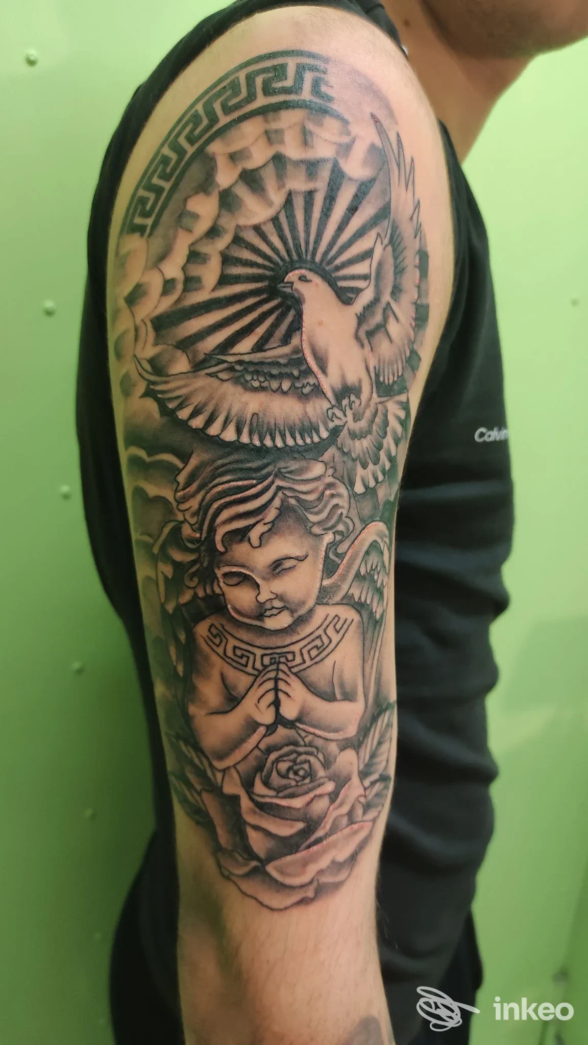 Tattoo realizzato sull'avambraccio sinistro, raffigurante una colomba al centro con raggi, decorazioni geometriche e una rosa, eseguito su pelle reale, in tonalità di grigio.