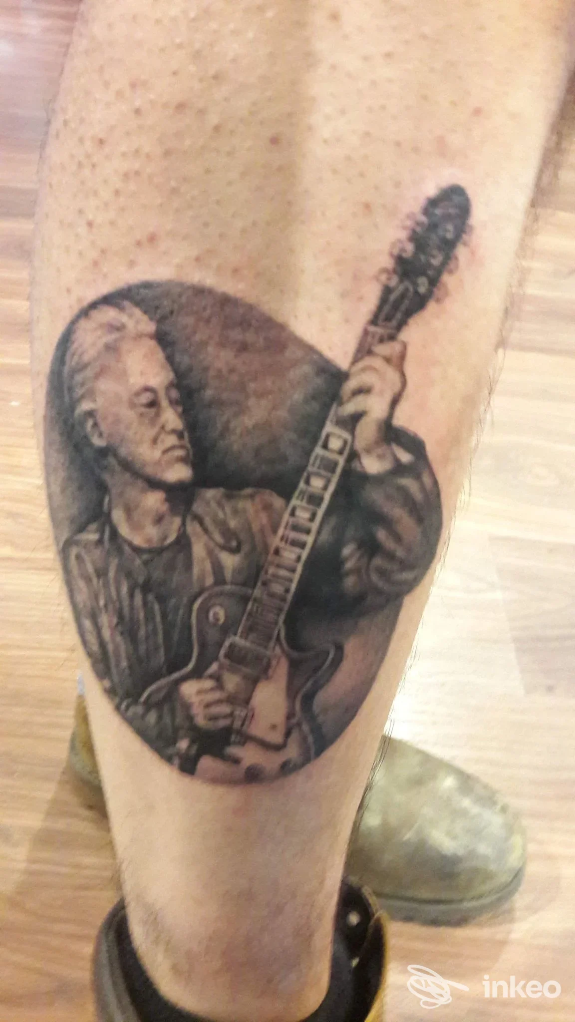 Tattoo realistico su avambraccio di una persona che suona una chitarra, con dettagli suttili e sfumato sullo sfondo.