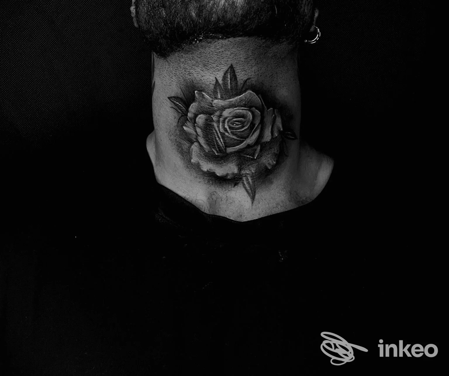 Rinforzo di una rosa tatuata sul collo di una persona, senza viso visibile, sfondo nero e fotografia in bianco e nero.