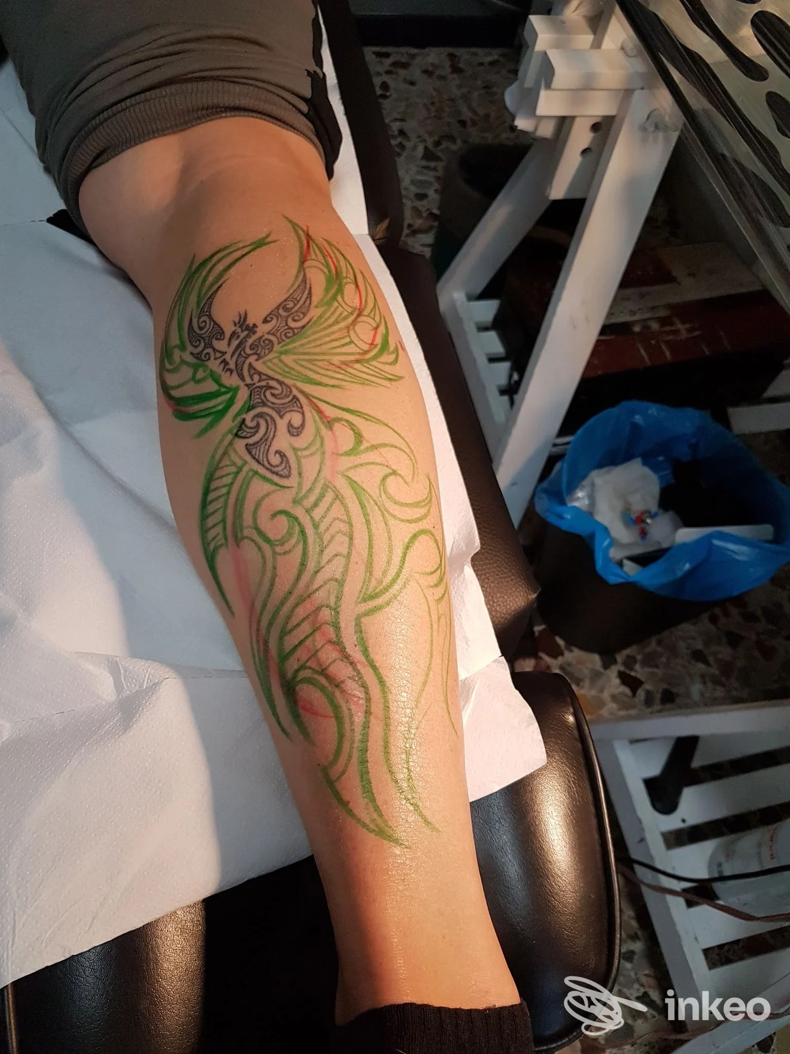 Tatuaggio verde su gamba, disegno stilizzato con forme organiche e ali, realizzato sulla pelle di una persona nel contesto dello studio Shark Tattoo a San Giuliano Milanese.
