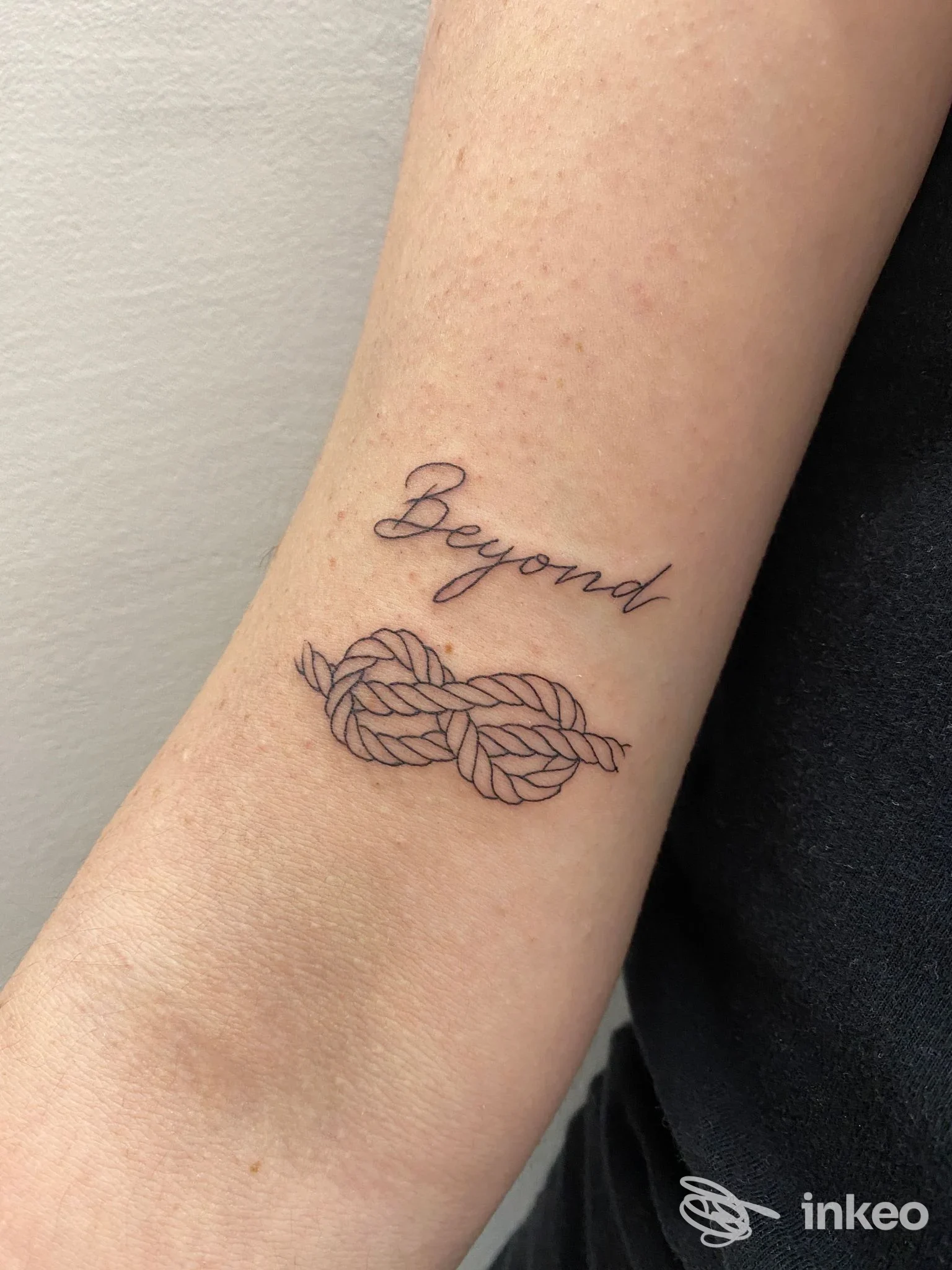 Avambraccio di una persona con tatuaggio: la parola Beyond in corsivo sovrastata da un nodo intrecciato, visibile sulla pelle.