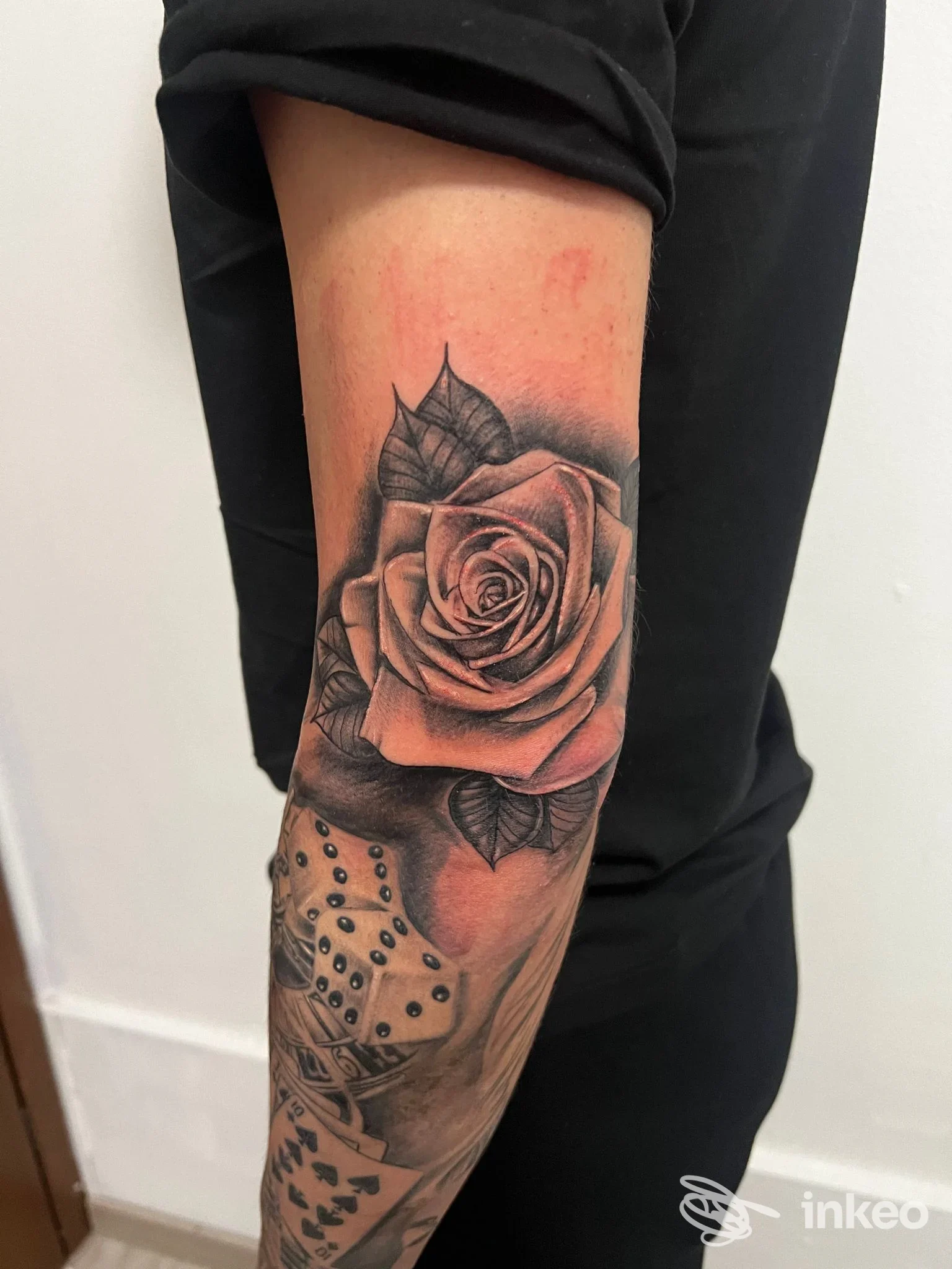 Tattoo realistico su avambraccio: una rosa dettagliata in tonalità scure, con gioco di sfumature e contorni netti, senza viso umano visibile.