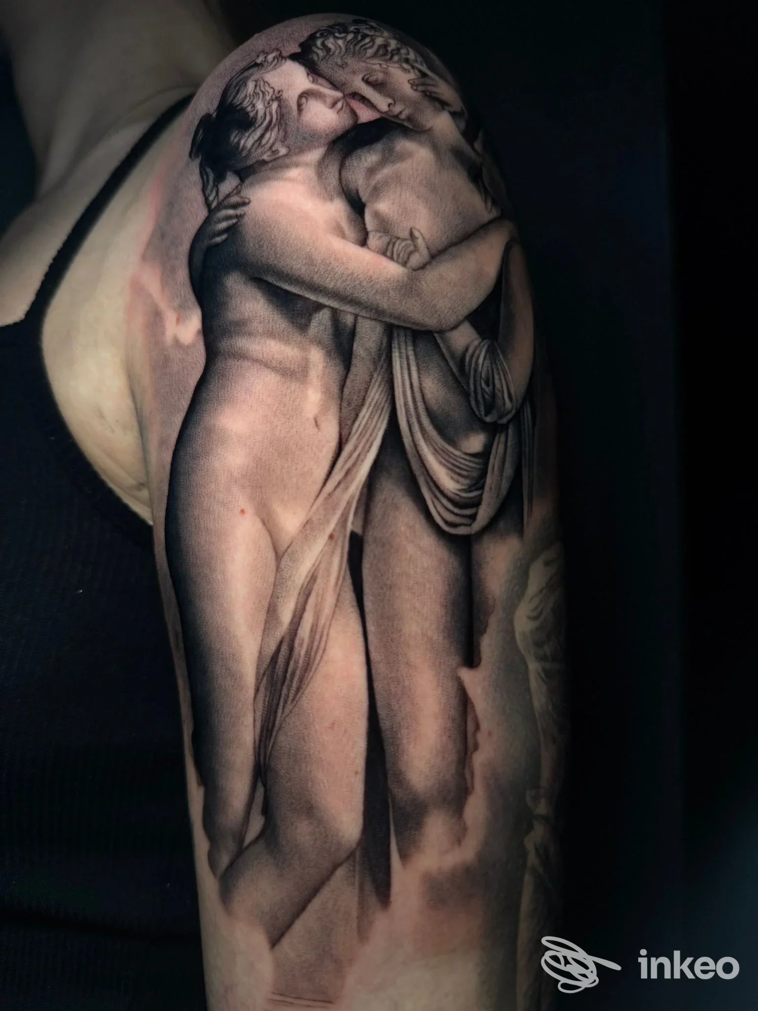 Tattoo realistico su braccio raffigurante due figure che si abbracciano, con tonalità scure e dettagli anatomici ben definiti.