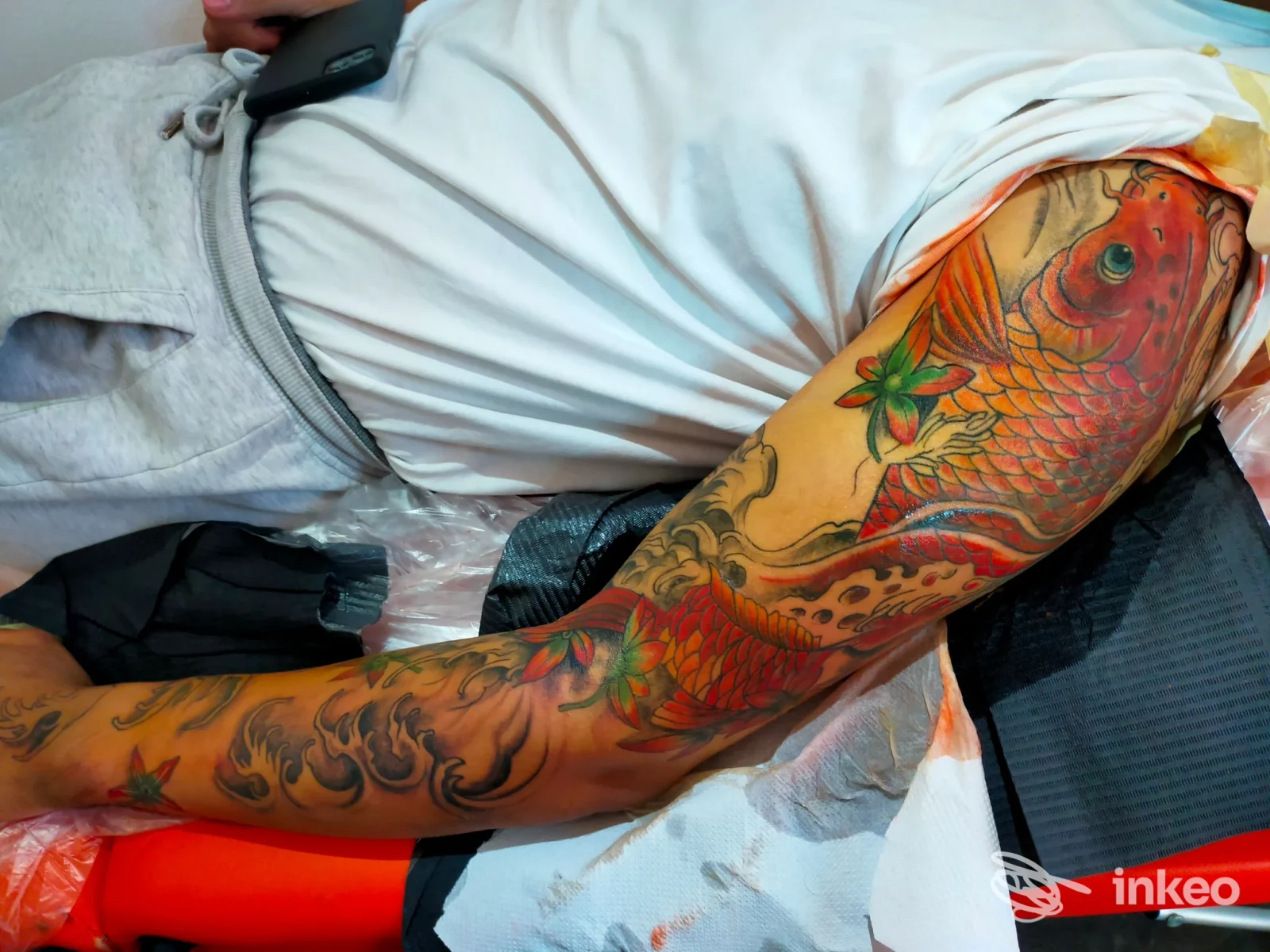 Tatuaggio colorato su braccio raffigurante un koi e fiori, realizzato sulla pelle di una persona, senza volto visibile e senza elementi di interfaccia. The Passion Art.