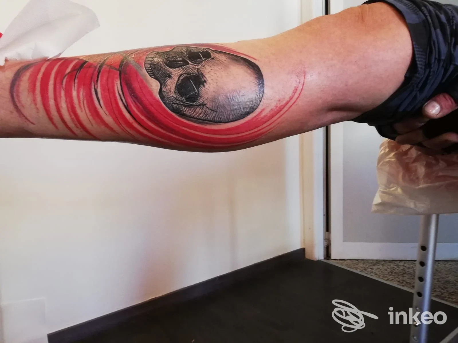 Brascio con tatuaggio a tema skull e linee rosse, realizzato sulla pelle del braccio, senza volti o elementi promozionali visibili.