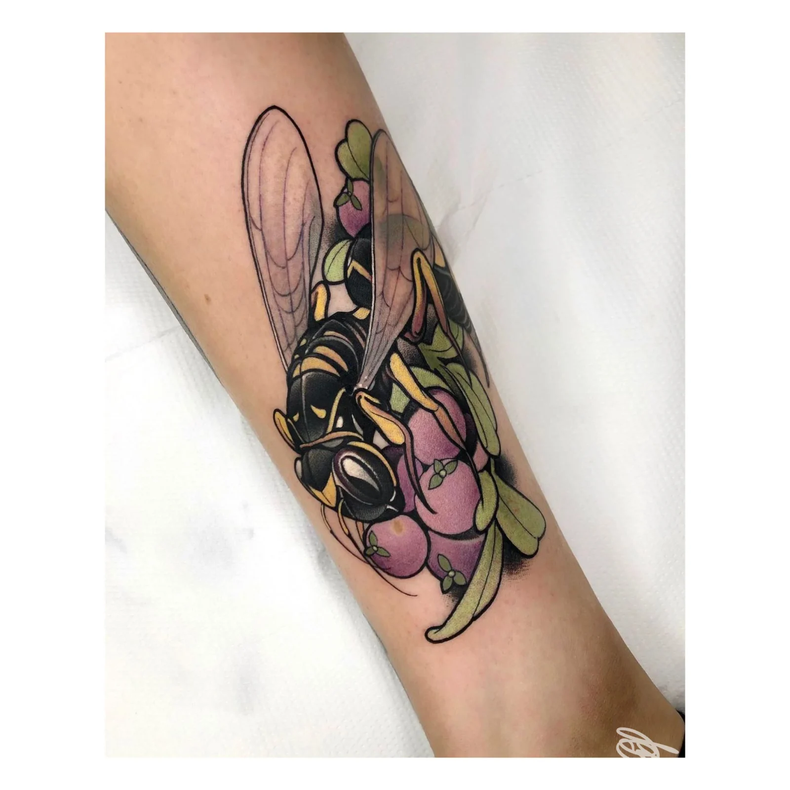 Tattoo colorato sull’avambraccio: insetto con ali nere e fiori colorati, realizzato sulla pelle reale; stile grafico vivace.