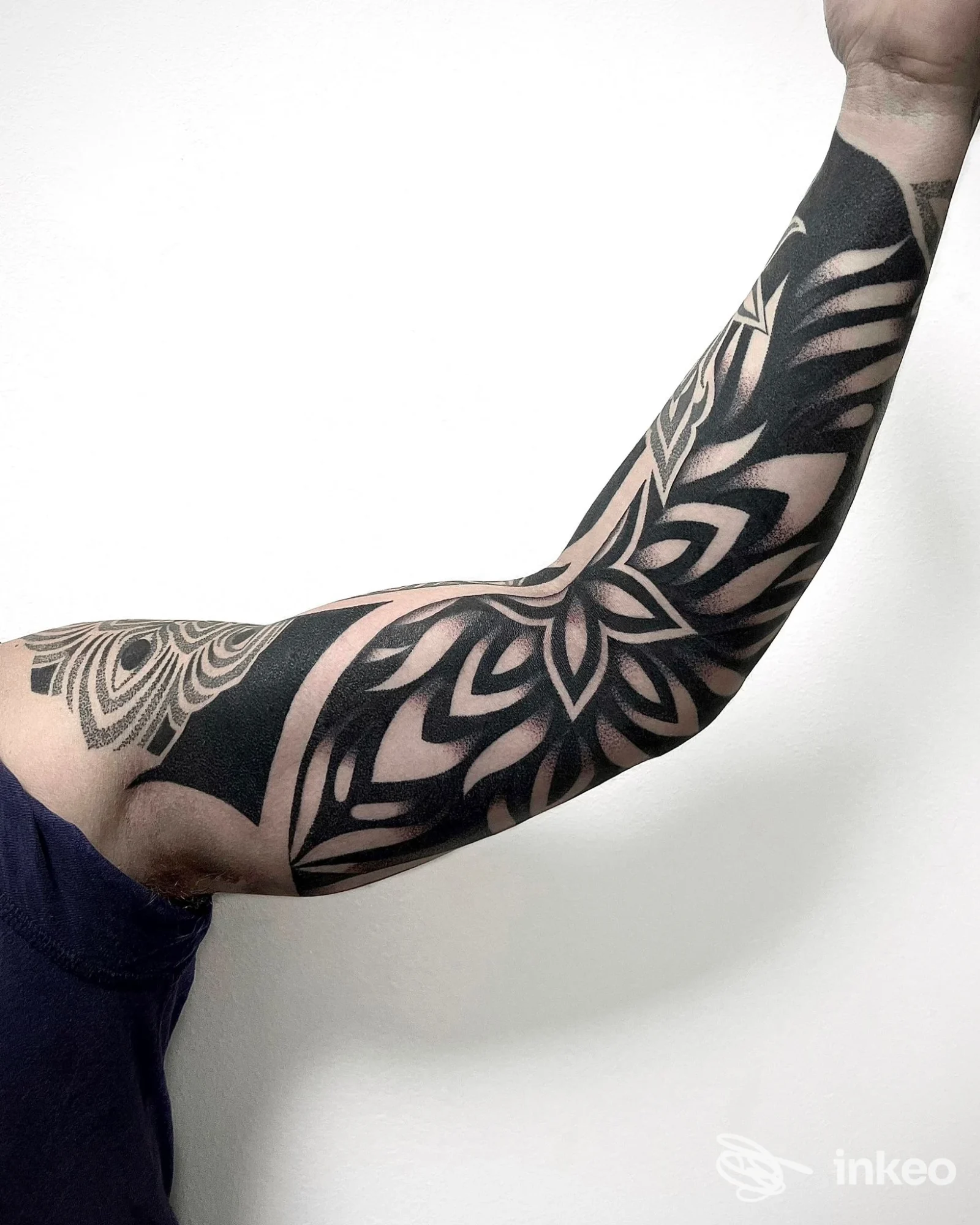 Braccio interamente coperto da un tatuaggio di stile mandala blackwork, visibile dall'avambraccio al braccio, senza volto nella foto, su sfondo chiaro.