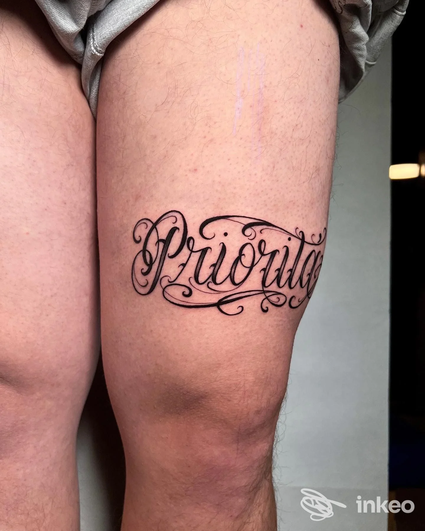 Tattoo calligrafico ornato sulla coscia, parola leggibile ma decorativa, realizzato sulla pelle.