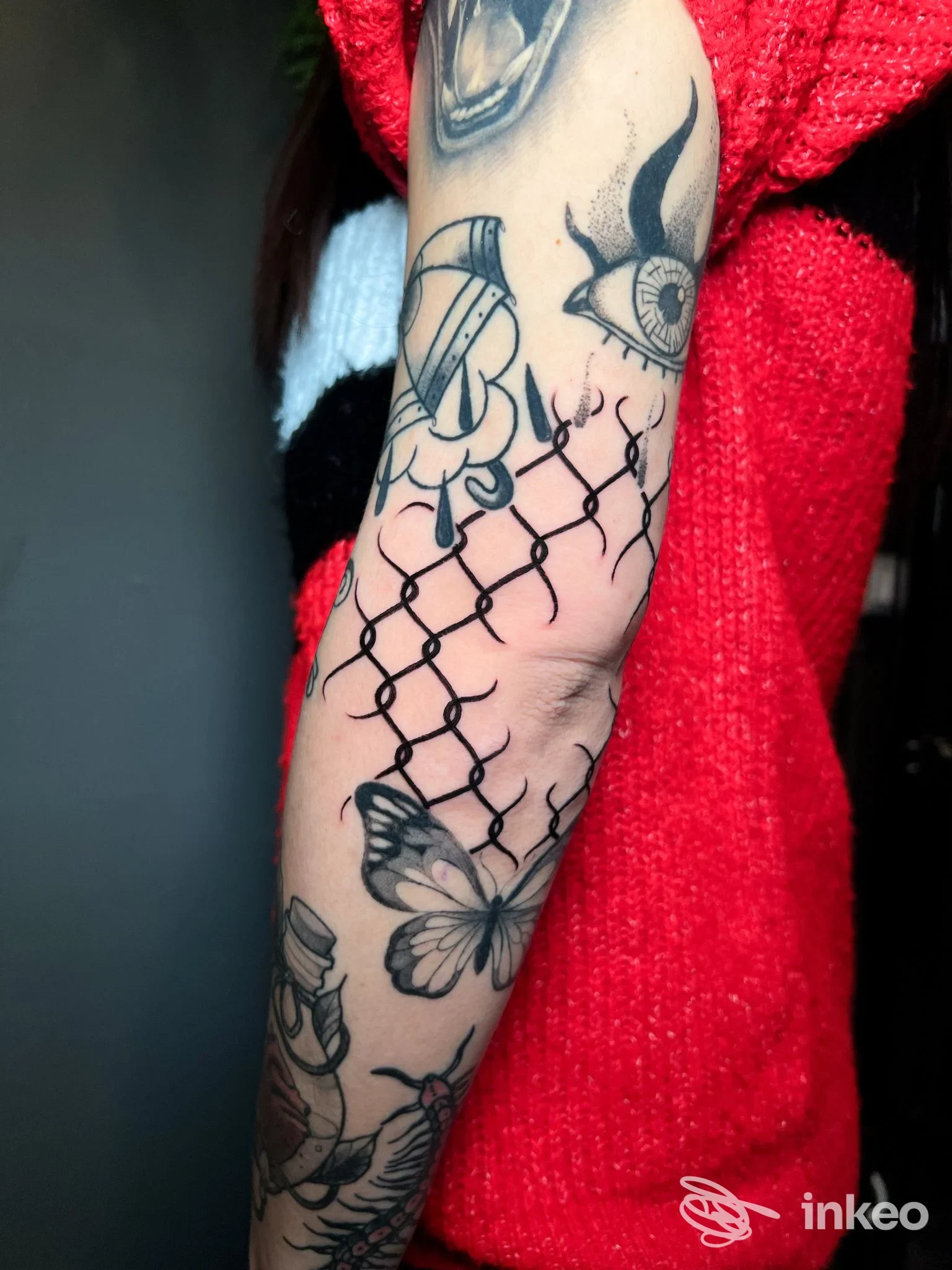 Tattoo visibile sull'avambraccio: reticolo a maglie con farfalla, inchiostro nero su pelle, senza volti visibili o elementi di overlay.