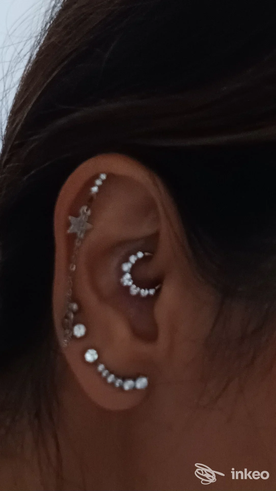 Orecchio di una persona con vari piercing: catene di piccole perle lungo l’elice, cerchio a forma di luna incastonato e una fila di perline lungo il lobo.