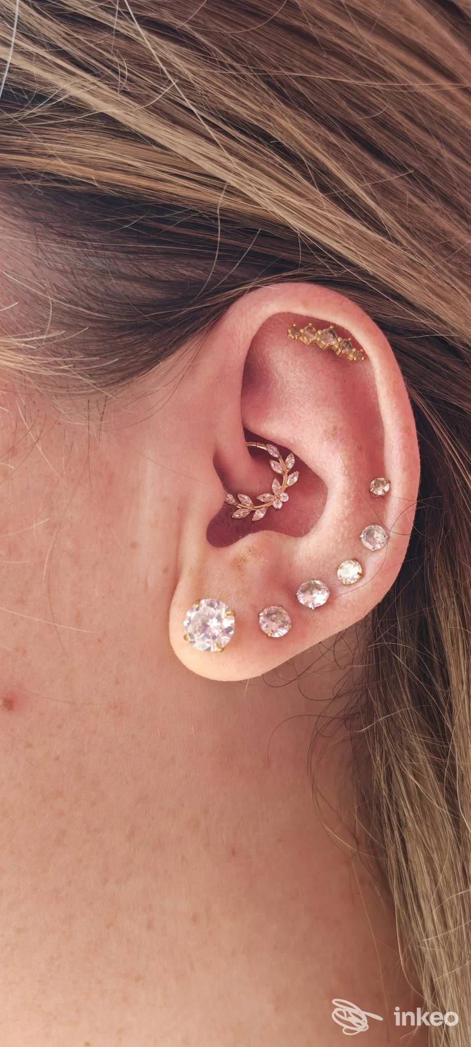 Primo piano dell'orecchio con multipli piercing: un grande brillantese nellobo esterno e una sequenza di brillanti lungo l'orecchio, con capelli che sfiorano. Studio Laei.