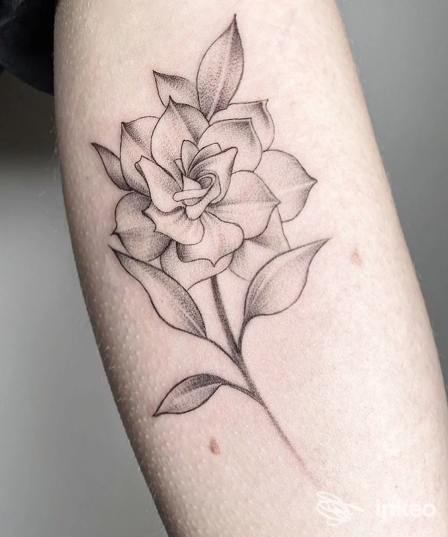 Tattoo su braccio raffigurante un fiore stilizzato in linee nere con dettagli di sfumatura, visibile in primo piano.