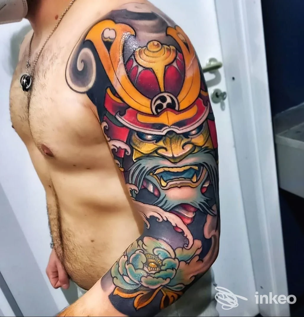 Braccio sinistro completamente tatuato con un pezzo colorato in stile giapponese, visibile sulla pelle: Samura e motivi floreali in manica, in un contesto studio fotografico.