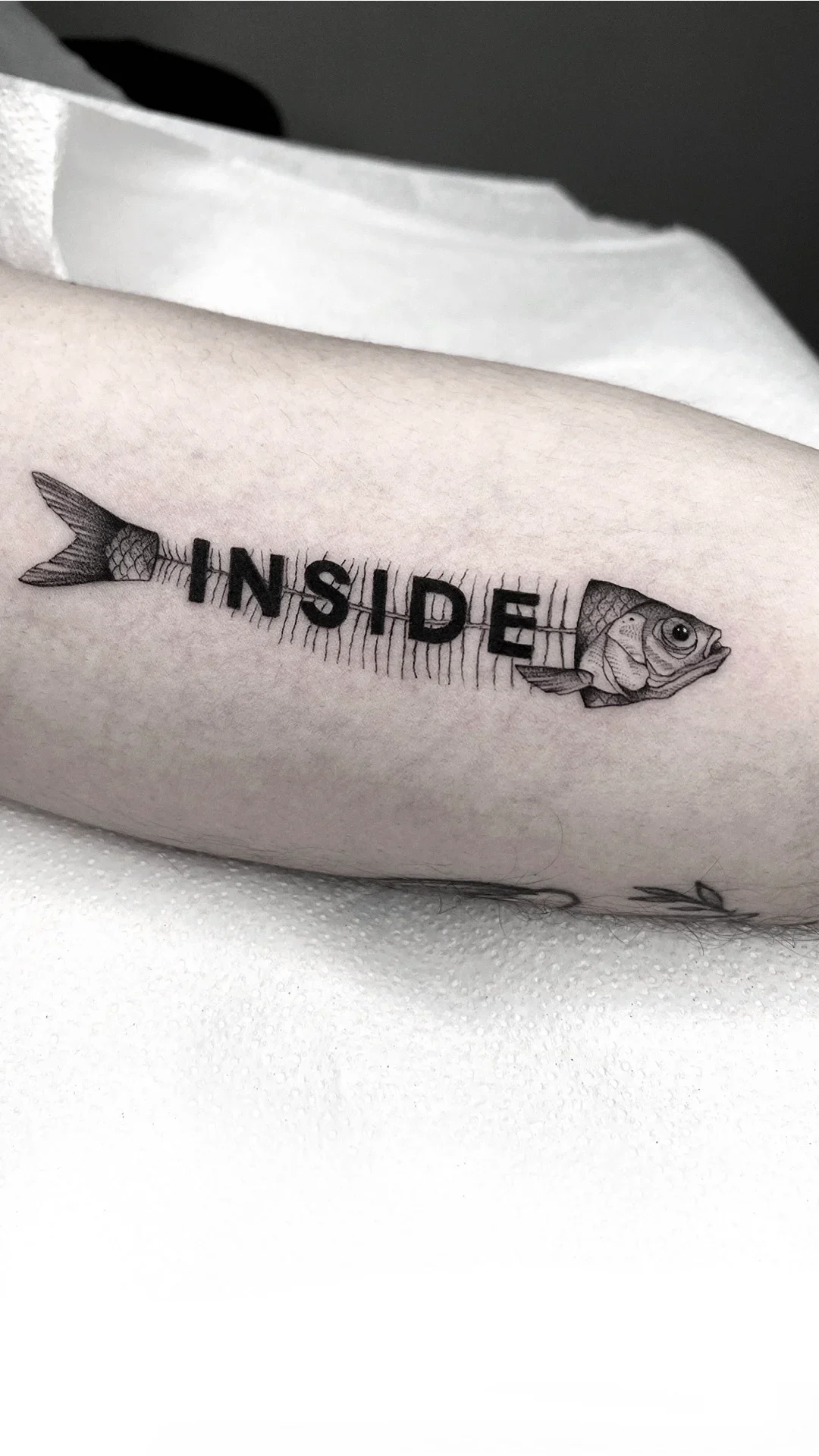 Tatuaggio su avambraccio: balena stilizzata con la parola INSIDE, disegnato direttamente sulla pelle.