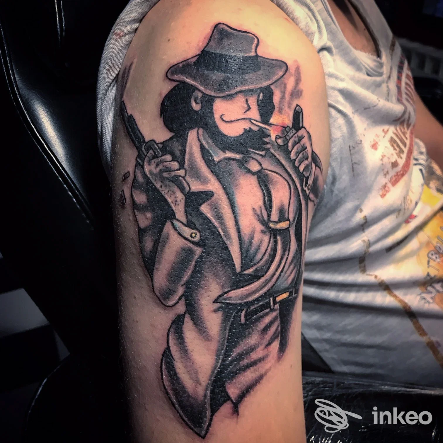 Tattoo raffigurante figura con cappello e pistola sull’avambraccio sinistro, in stile noir, realizzato sulla pelle.