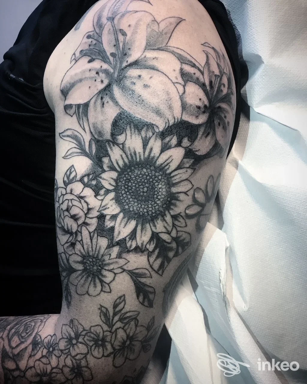 Tattoo floreale in bianco e nero sul braccio, fiore grande al centro con altri fiori lungo la parte esterna, pelle umana visibile senza volto.