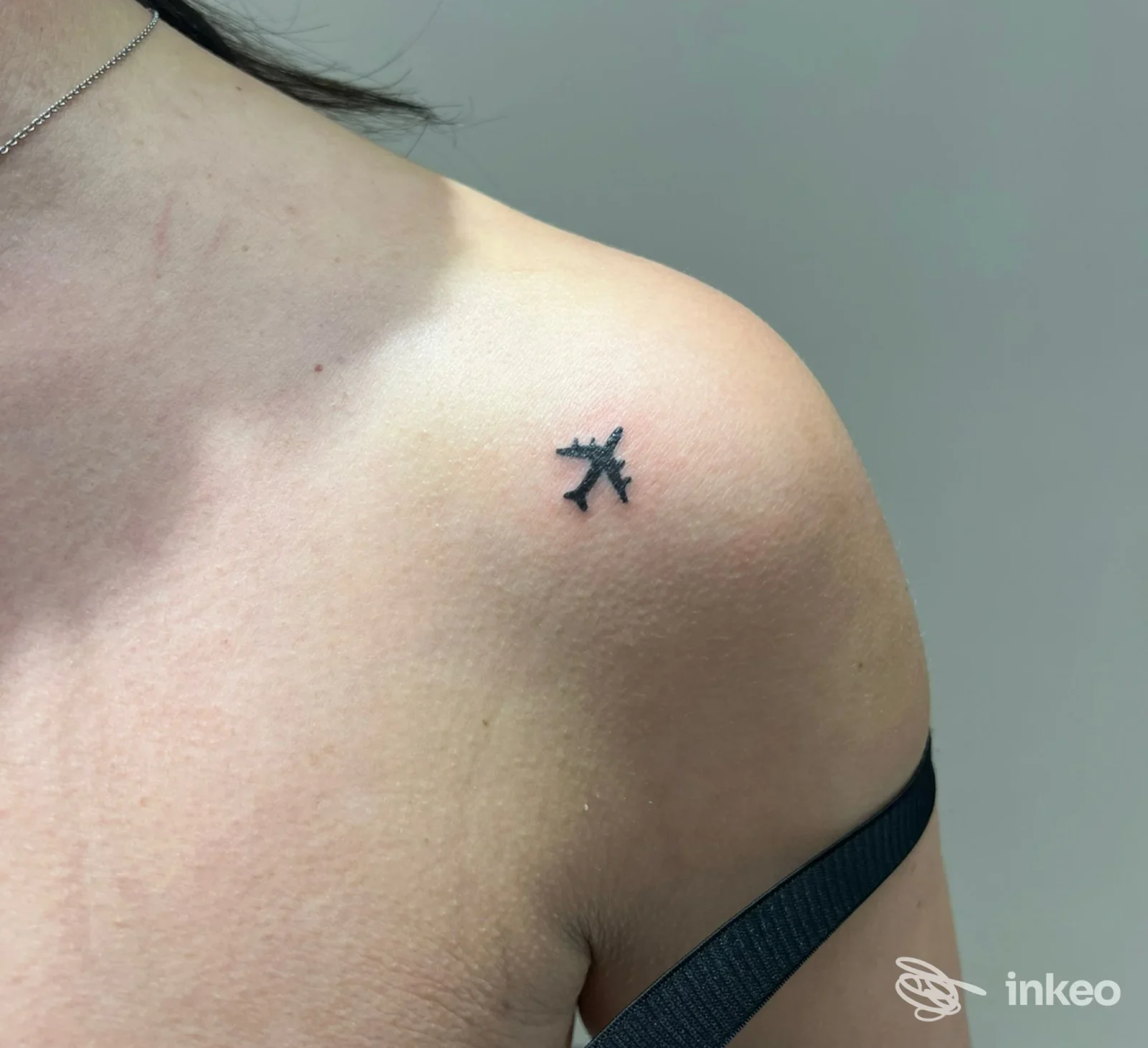 Tattoo aeroplano nero sulla spalla destra, visibile su pelle, foto singola senza testo aggiunto o watermark, studio DOINELLÉ.