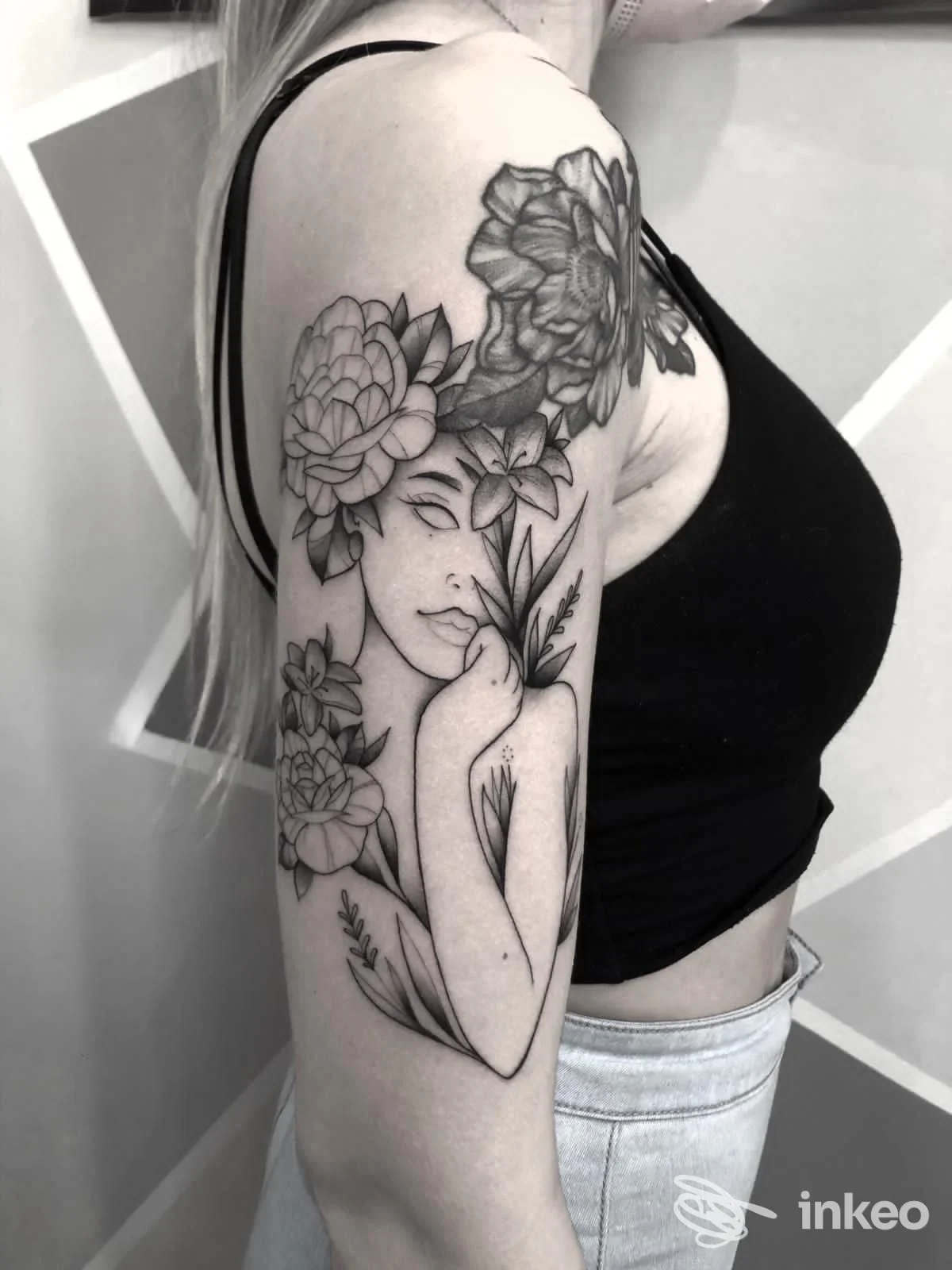Tattoo in bianco e nero sul braccio sinistro raffigurante una donna avvolta da fiori, visibile su una persona in top nero; inquadratura pulita senza overlay. Studio Noir Tattoo Studio.