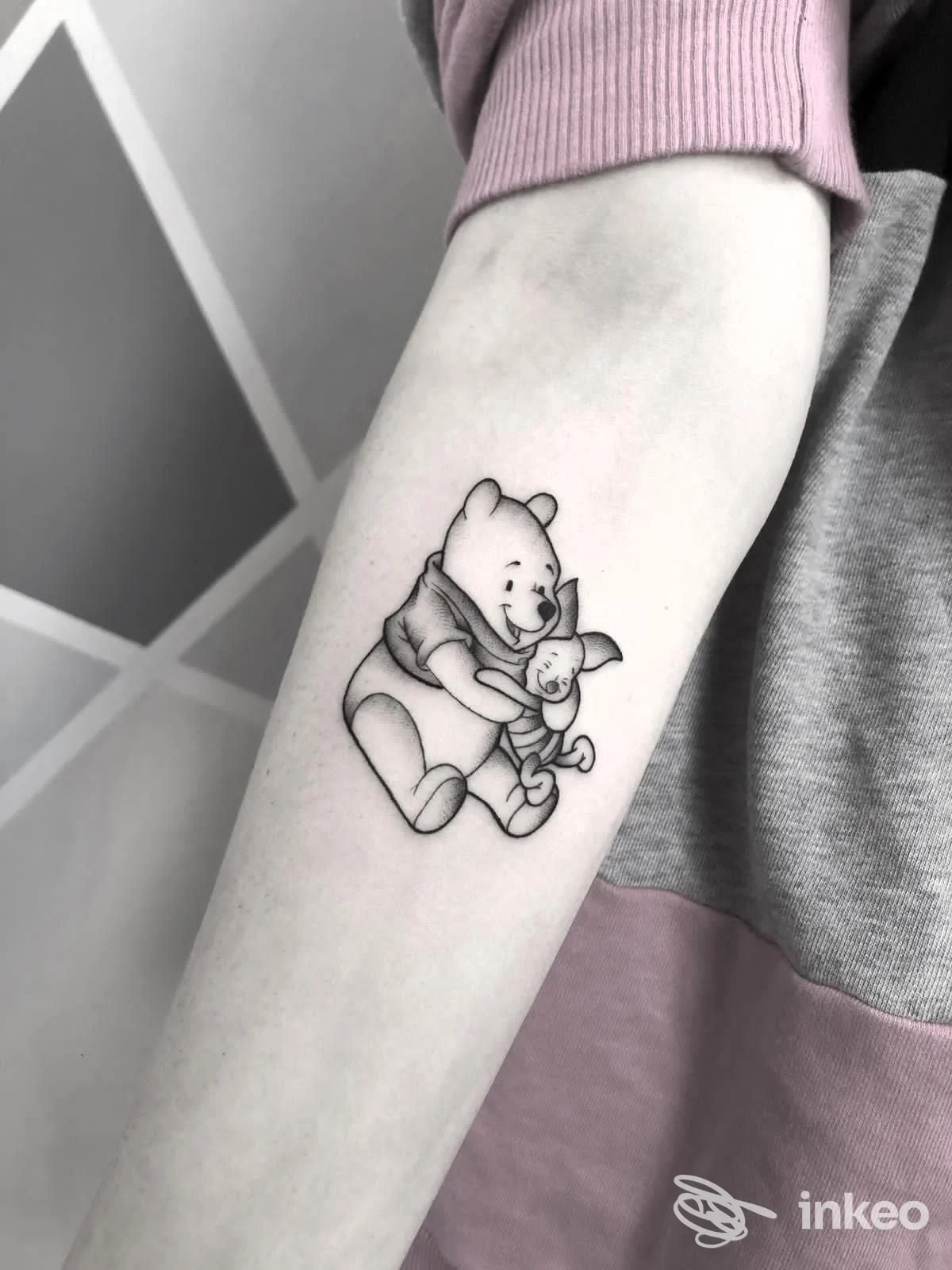 Tattoo raffigurante Winnie the Pooh abbracciando un coniglio sull'avambraccio di una persona, realizzato su pelle umana senza elementi di overlay o testo esterno.