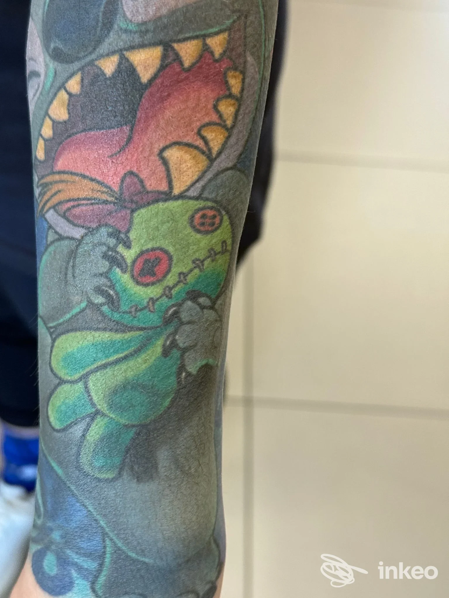 Tattoo colorato su un braccio, ritratto di una creatura verde con contorni netti; alcun volto umano visibile. Studio Memorink Tattoo Studio.
