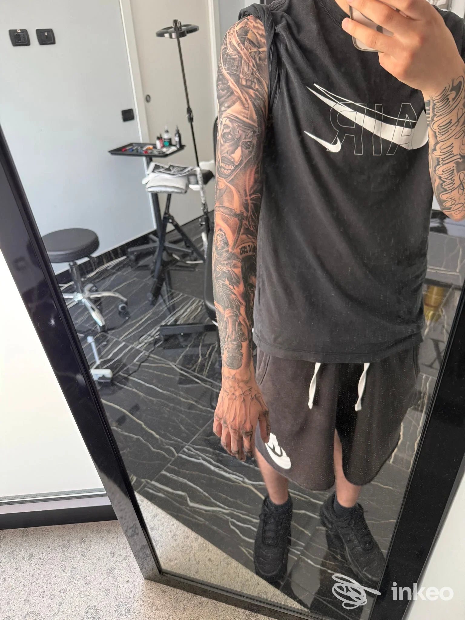Veduta frontale di una persona che mostra estesi tatuaggi sulle braccia in uno studio, abbigliamento sportivo, sembra una foto di persa con arm sleeves visibili