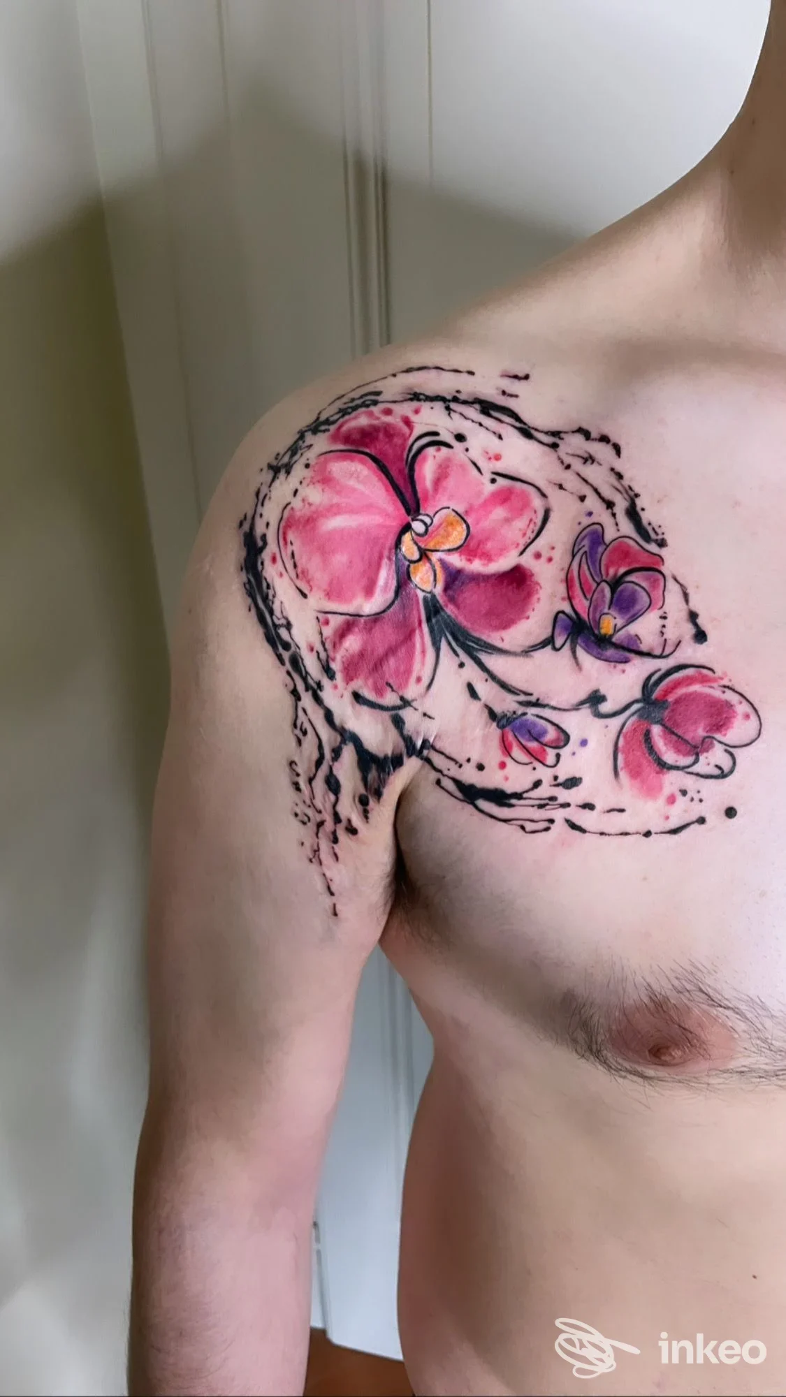 Tattoo floreale colorata sulla spalla e parte del torace di un uomo, con contorni neri marcati e sfumature rosa e viola.