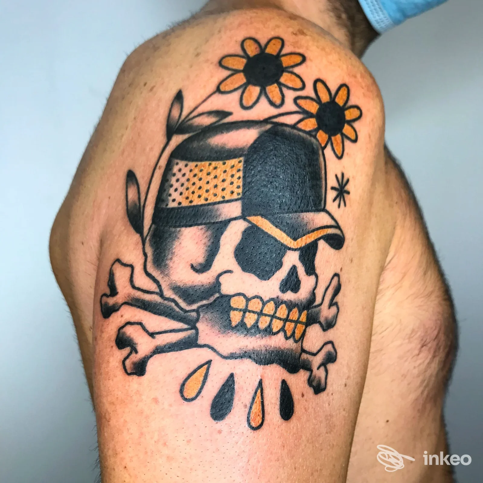Tattoo su braccio raffigurante teschio con cappello, ossa incrociate e fiori gialli, colori vividi su pelle. studio J INK Tatuaggi (luogo non specificato).