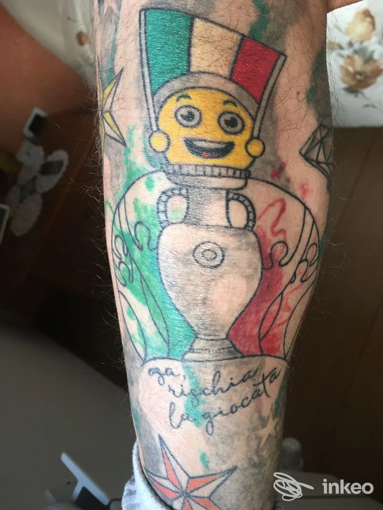 Tatuaggio sul braccio raffigurante una figura gialla con cappello tricolore e un vaso, colori vivaci e contorni definiti.