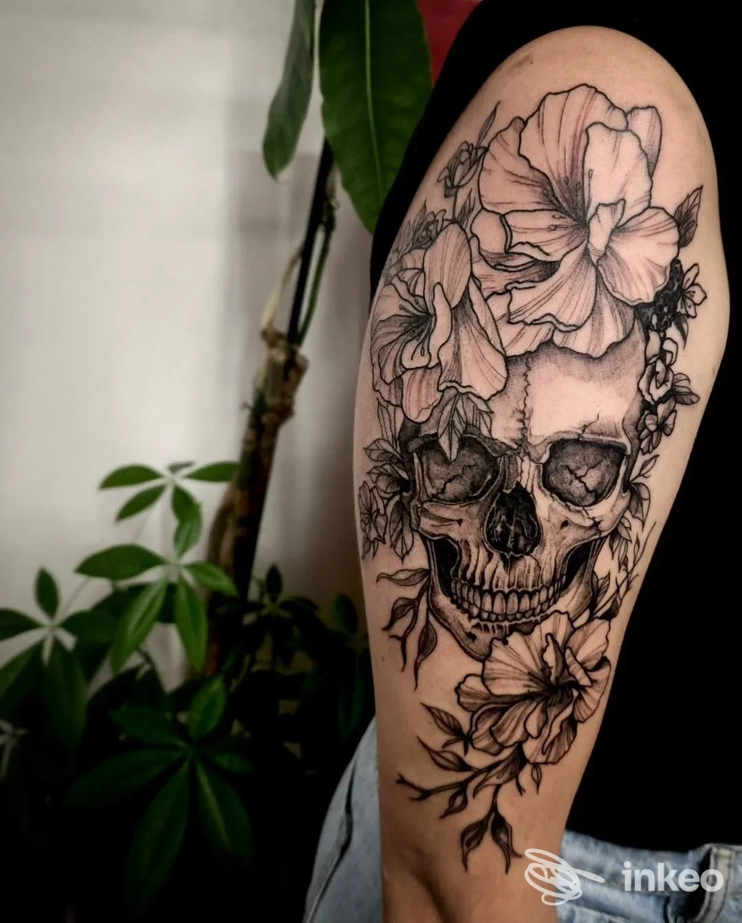 Tatuaggio realistico a tema teschio e fiori stampato sulla pelle di un braccio, in bianco e nero, senza presenza di volto umano.